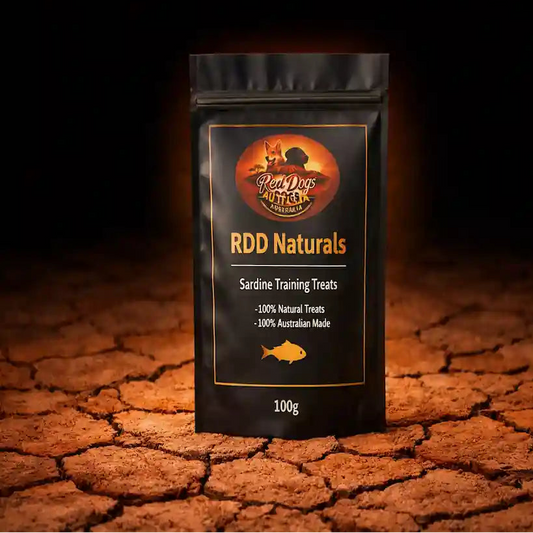 A black stand-up pouch of RDD Naturals Sardine Training Treats stands on cracked earth against a dark background. The pouch has a gold and orange logo and text, with a small 'Made with AI' badge in the top right corner.