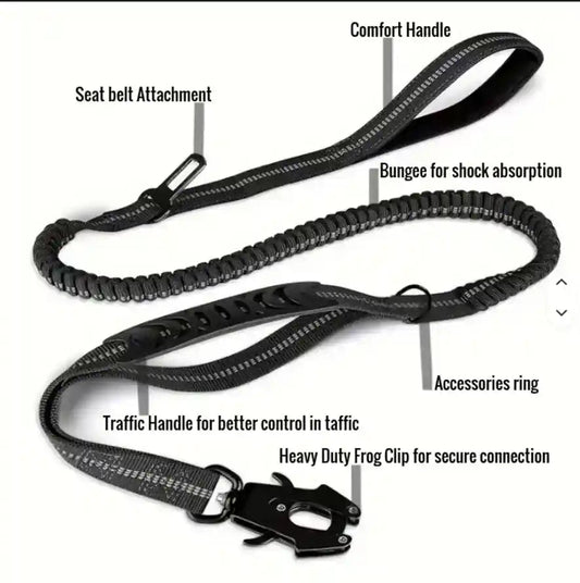 A black dog leash with multiple labeled callouts showing features such as seat belt attachment, comfort handle, bungee for shock absorption, accessories ring, traffic handle, and heavy duty frog clip, on a plain white background.