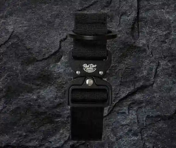 A black tactical belt with a black metal buckle featuring a white 'Red Dog Tactical' logo, displayed against a dark textured slate background.
