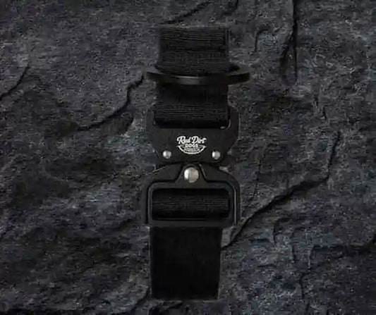 A black tactical belt with a black metal buckle featuring a white 'Red Dog Tactical' logo, displayed against a dark textured slate background.