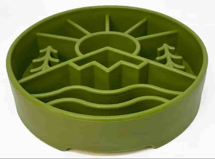 An olive green silicone pet slow feeder bowl with a landscape design featuring a sun, mountains, trees, and wavy water lines, shown on a plain white background.