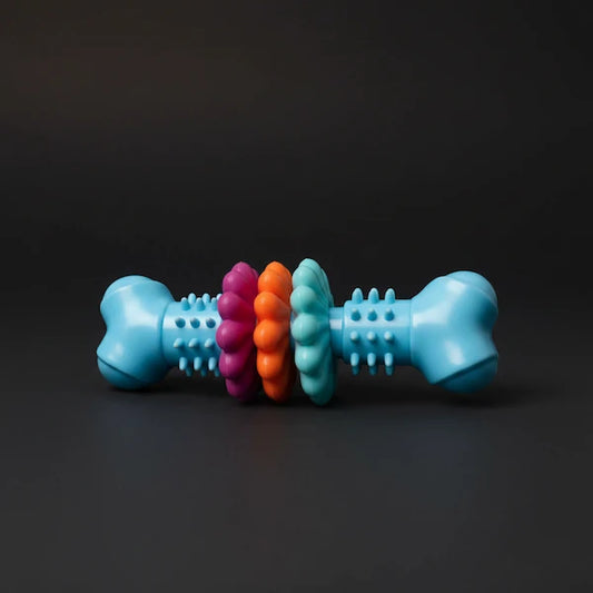 A bone-shaped dog toy with textured sides and three colorful inner rings in pink, orange, and teal, set against a dark gray background.