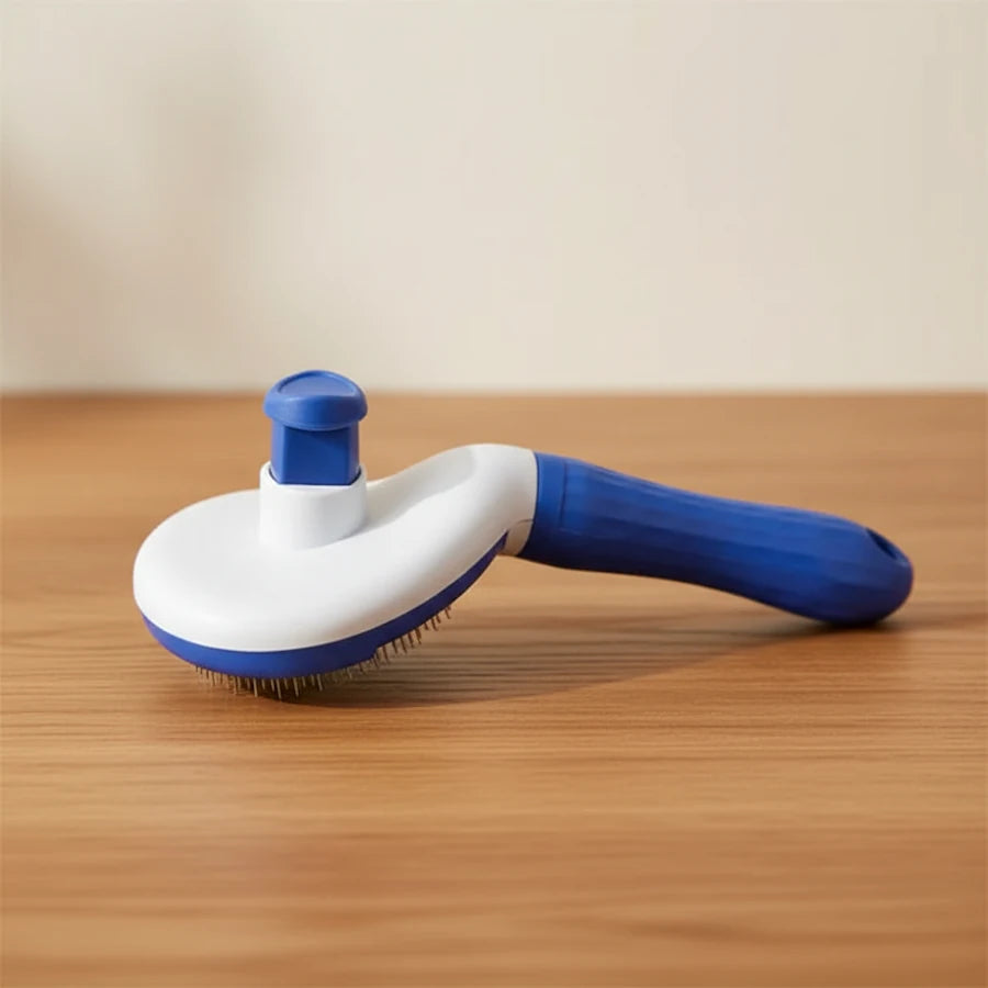 A blue and white pet grooming brush with a flexible bristle head and a curved handle, resting on a wooden tabletop against a neutral beige background.